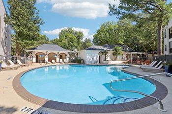 A large outdoor swimming pool surrounded by trees and lounge chairs.